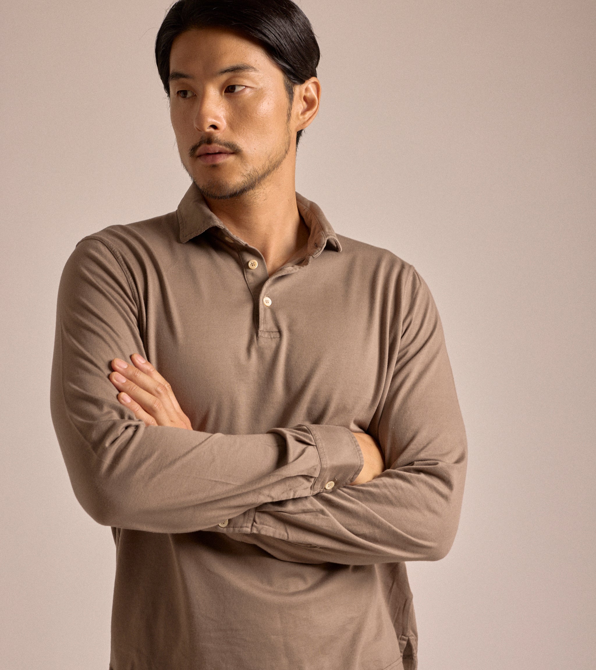 Model wearing the Fedeli Zero Cotton Jersey Long Sleeve Polo in dark greige. Front view with his arms crossed.