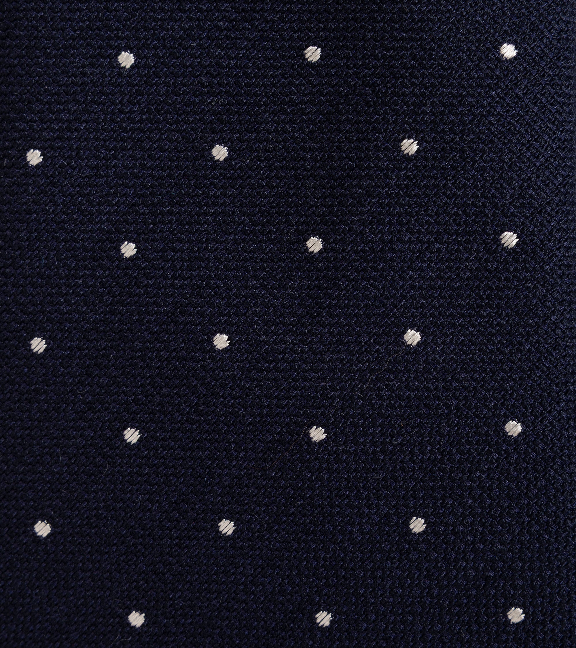 A close-up of a navy blue knit fabric with a repeating pattern of small white polka dots.