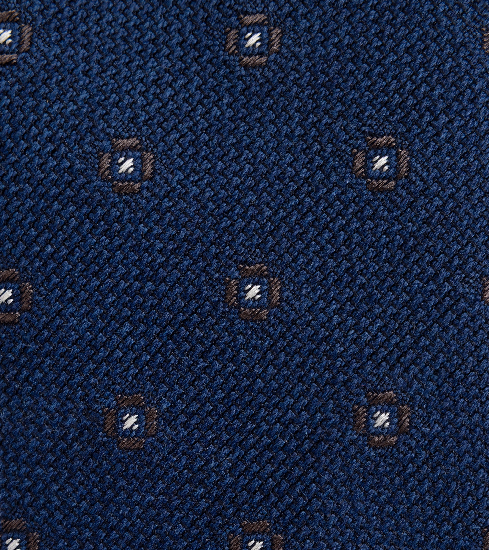 A close-up of a textured navy blue woven fabric with a repeating small medallion pattern in brown and white.