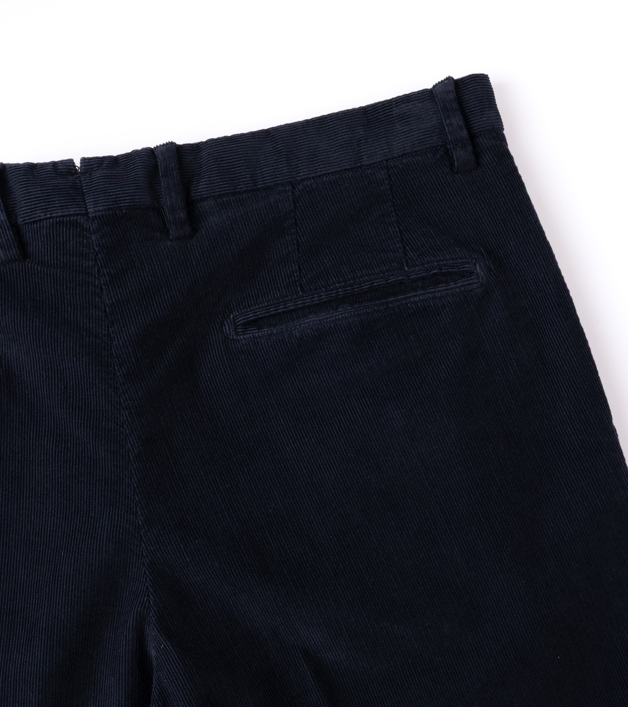 Close-up of the back waistband and pocket area of navy blue corduroy trousers on a white background.