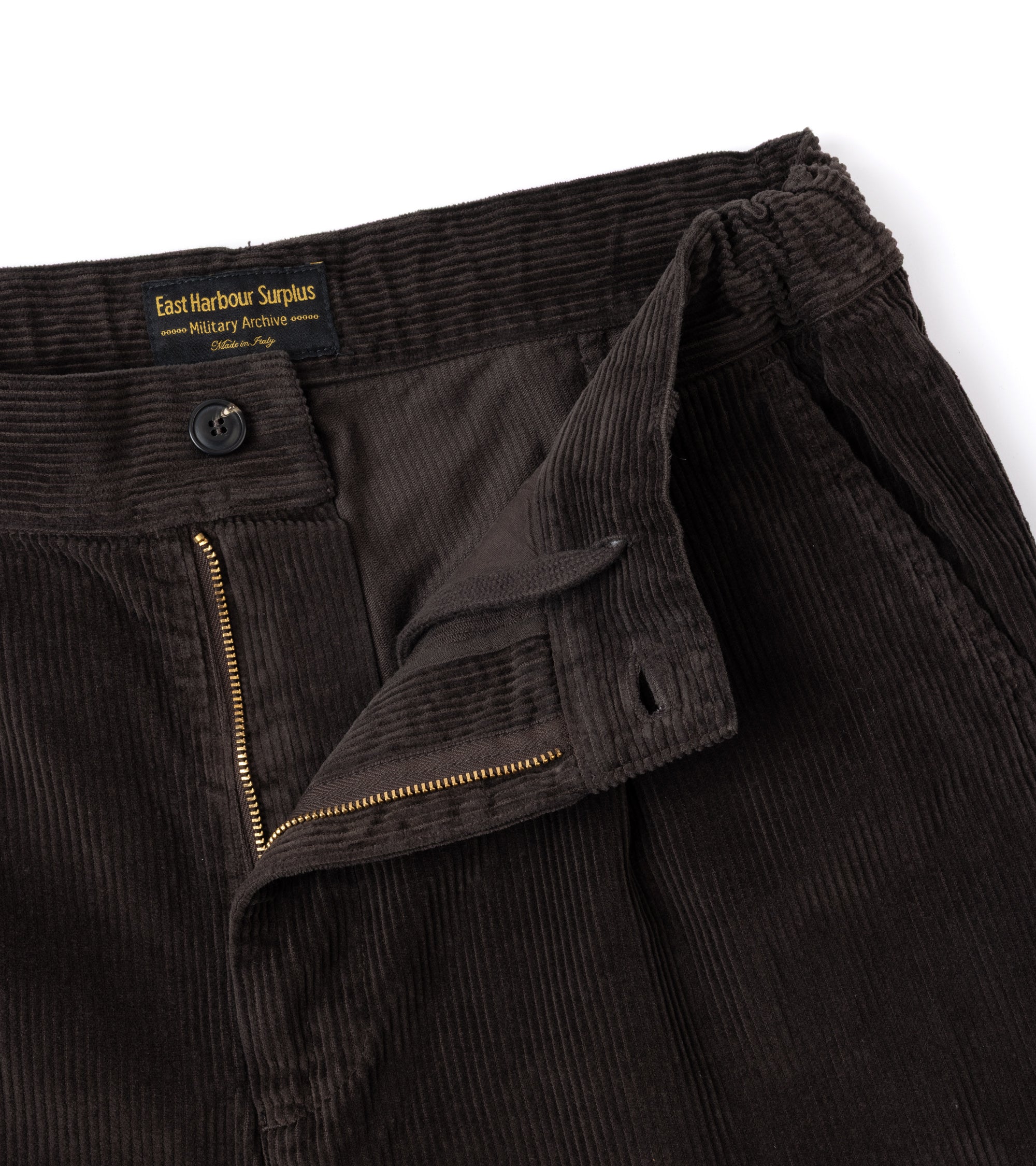 Close-up of brown corduroy trousers showing the waistband, button closure, zipper and inner drawstring.
