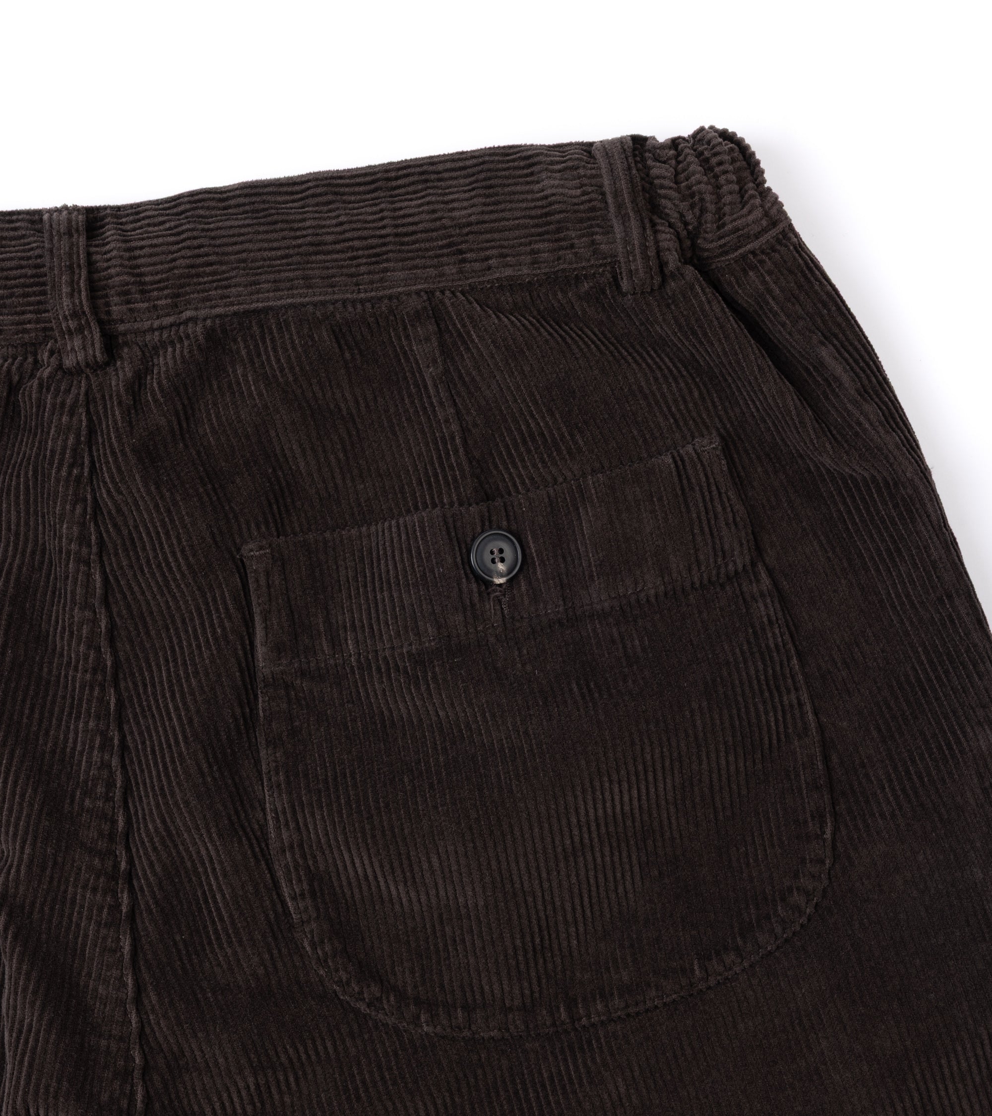 Close-up of dark brown corduroy trousers showing the back pocket with a button closure and the ribbed fabric texture.