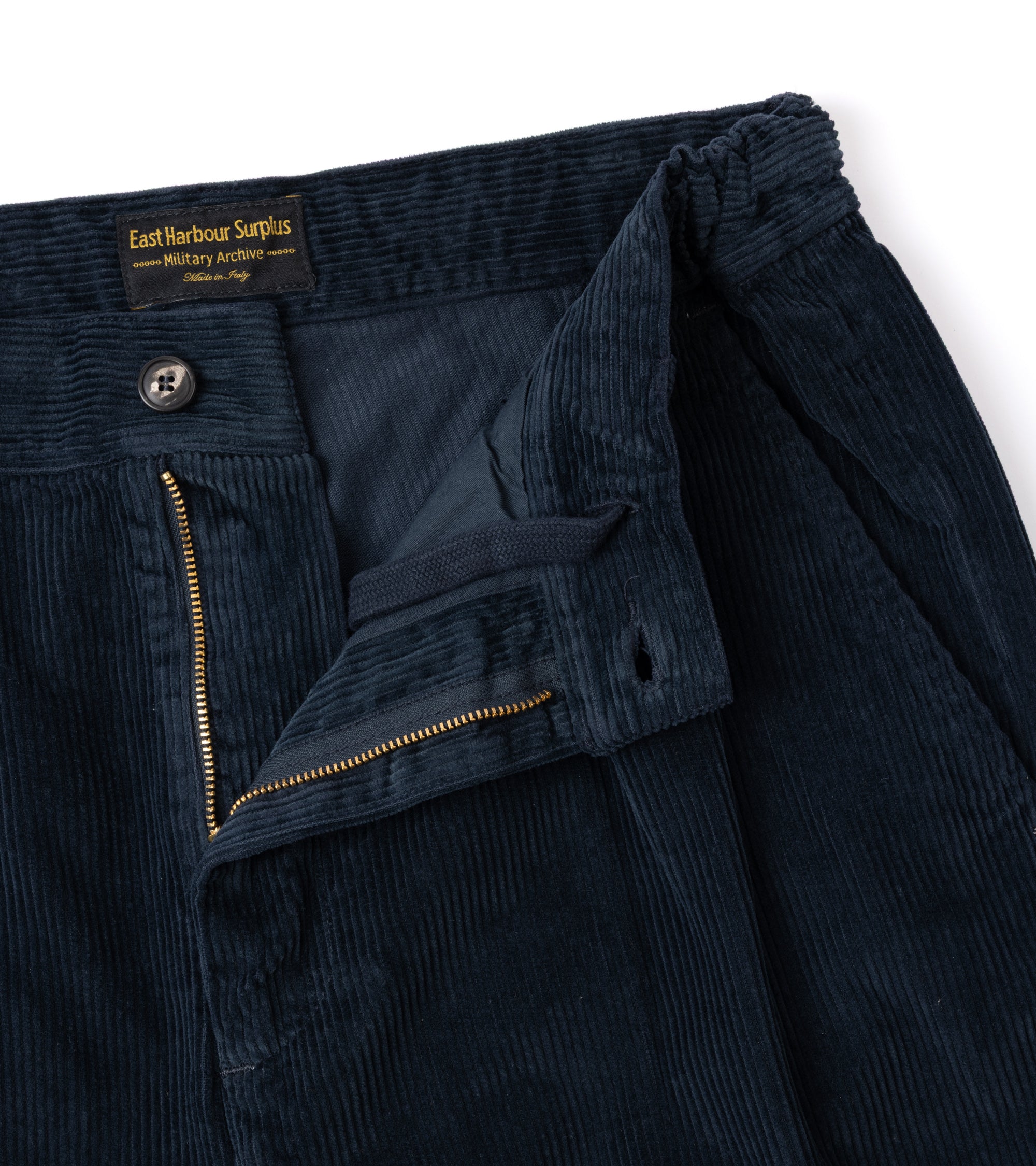 Close-up of dark navy corduroy trousers showing the waistband, button closure, front zip and inner drawstring.