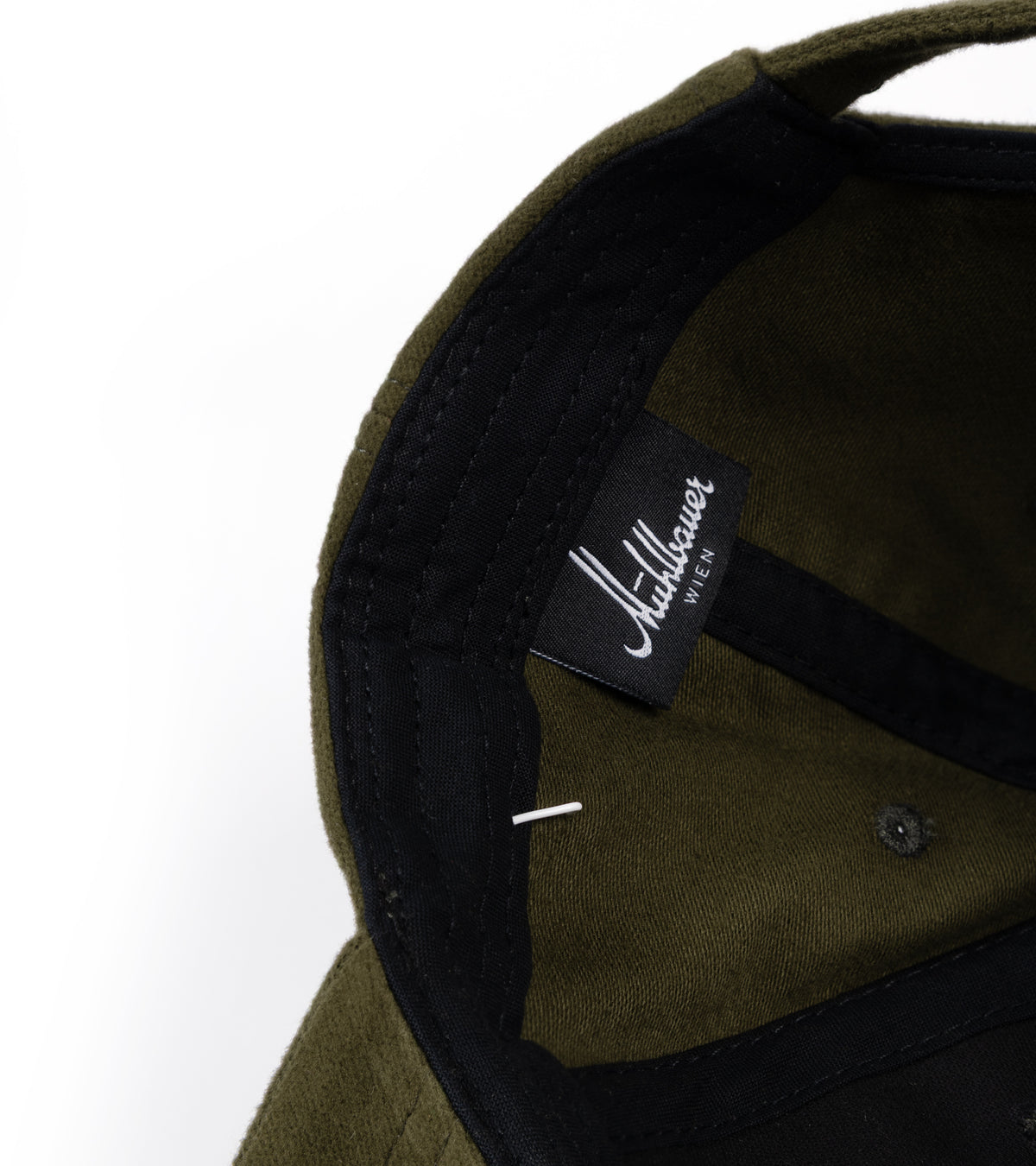 Close-up detail of a structured cap's interior, showing an olive green fabric crown with black contrast trim and a black interior label.