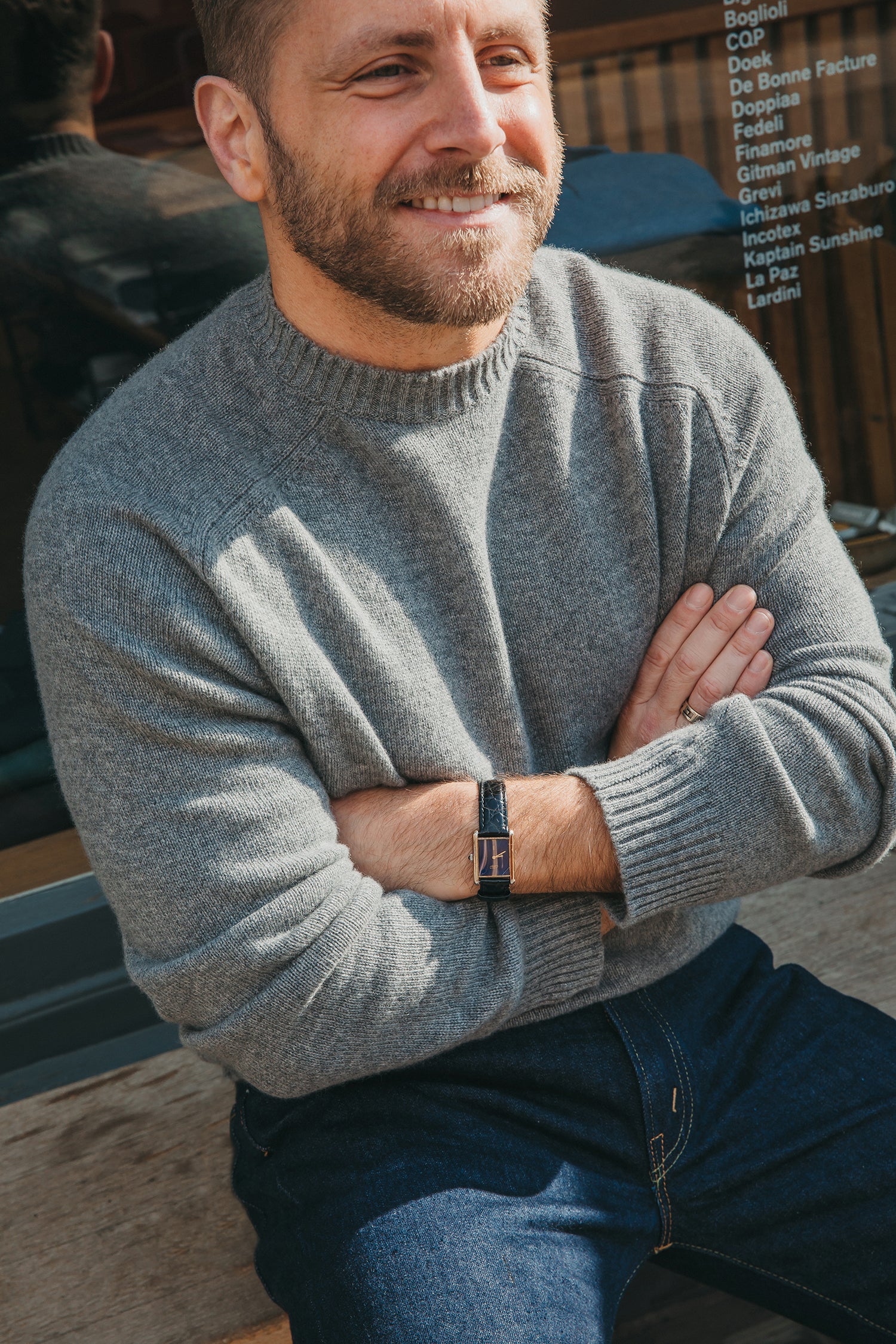 Man wearing a gray cashmere sweater with arms crossed, sitting outdoors.