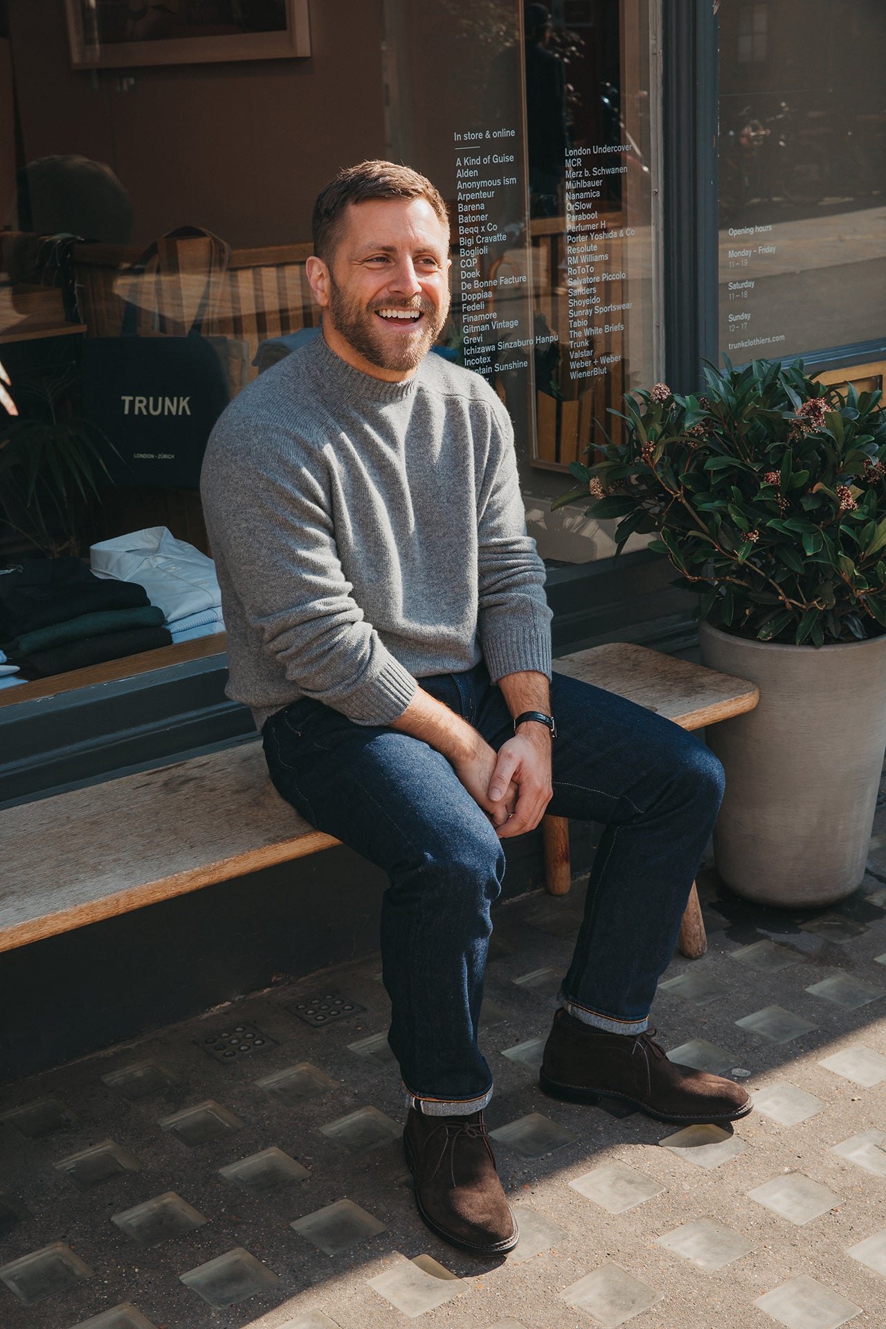 Man sitting on a bench outside a store with a plant in the background