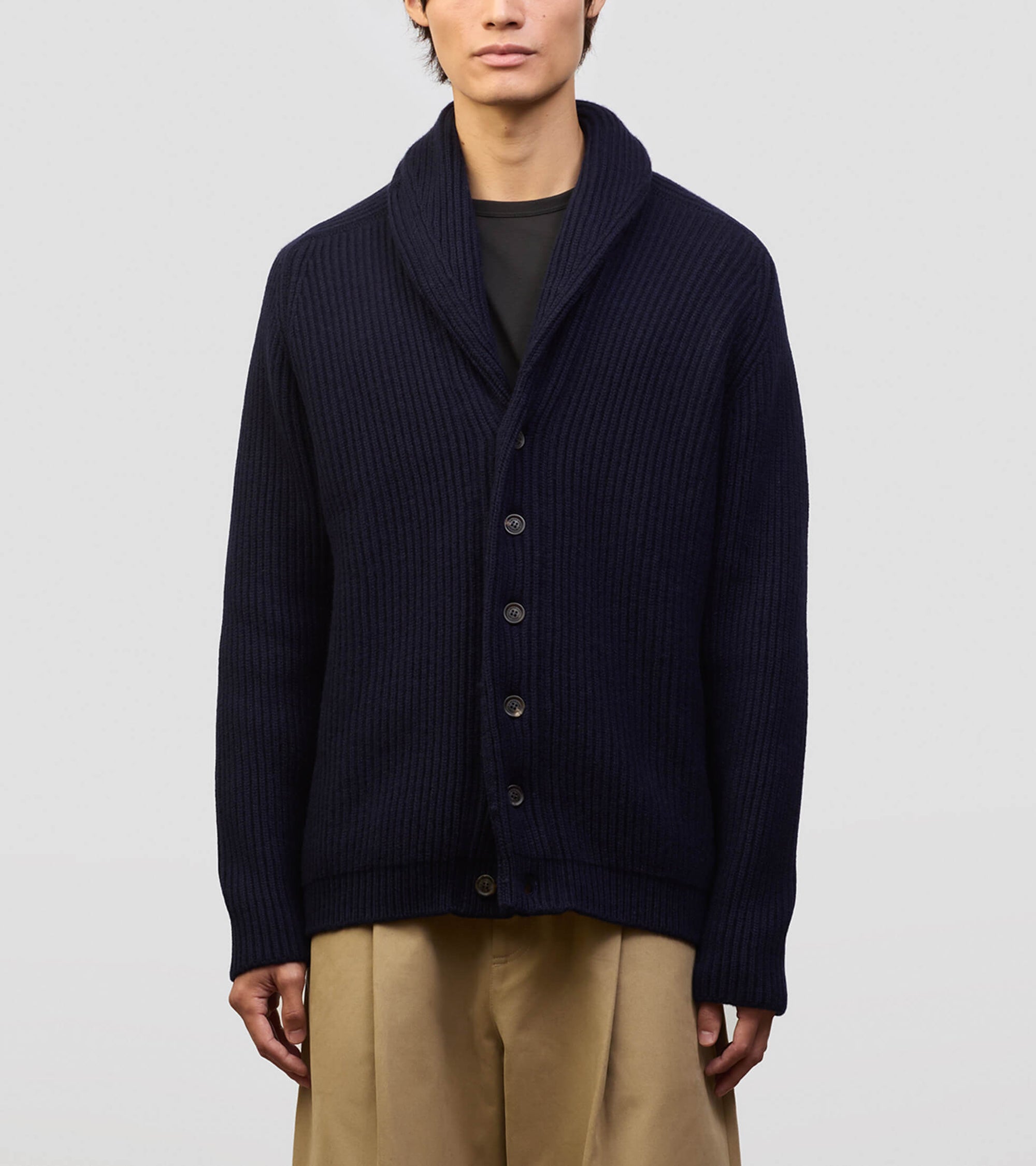 Person wearing a dark blue cardigan over a black shirt with beige pants on a light gray background
