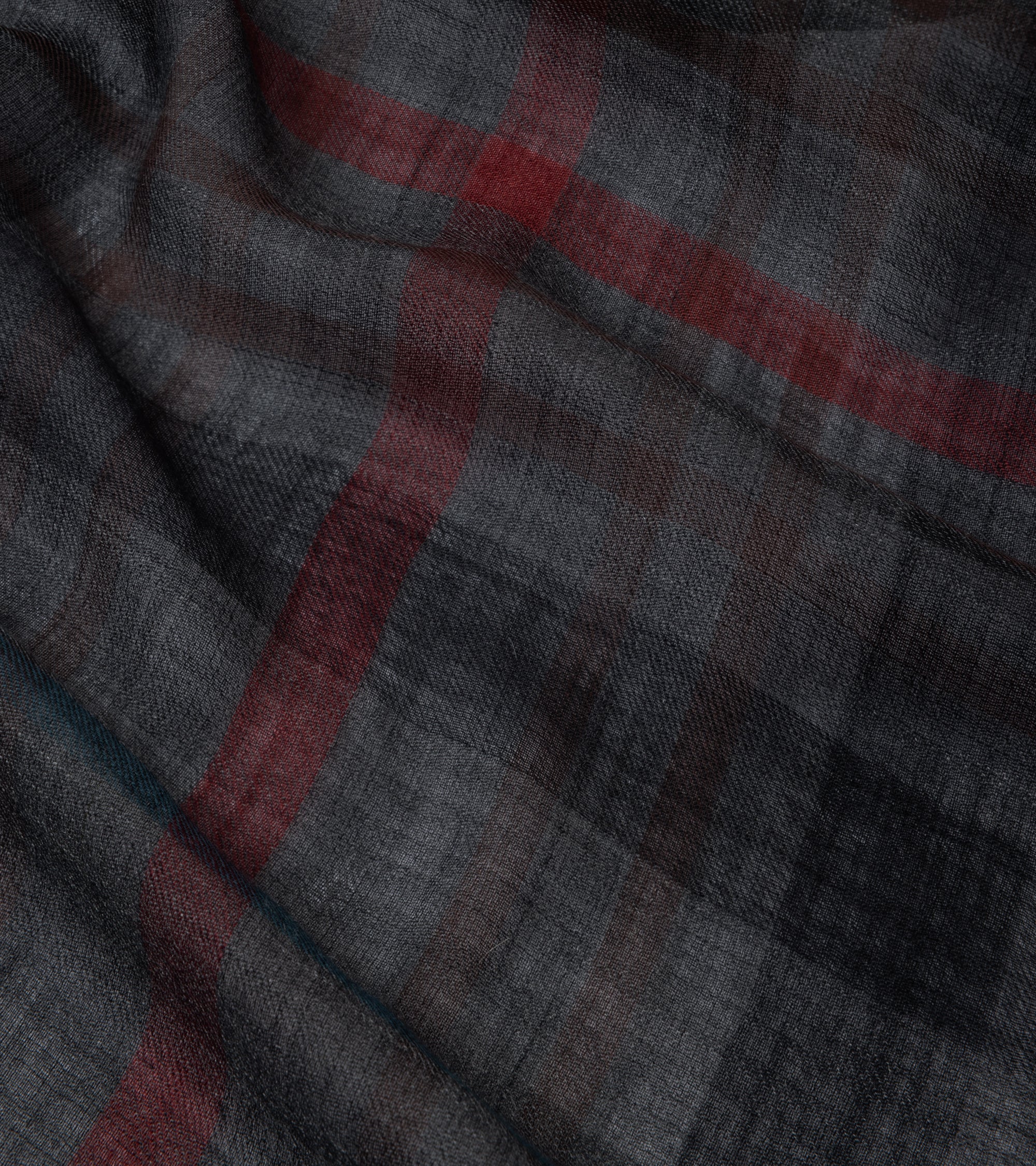 A close-up of a plaid charcoal fabric with red and teal accent lines,