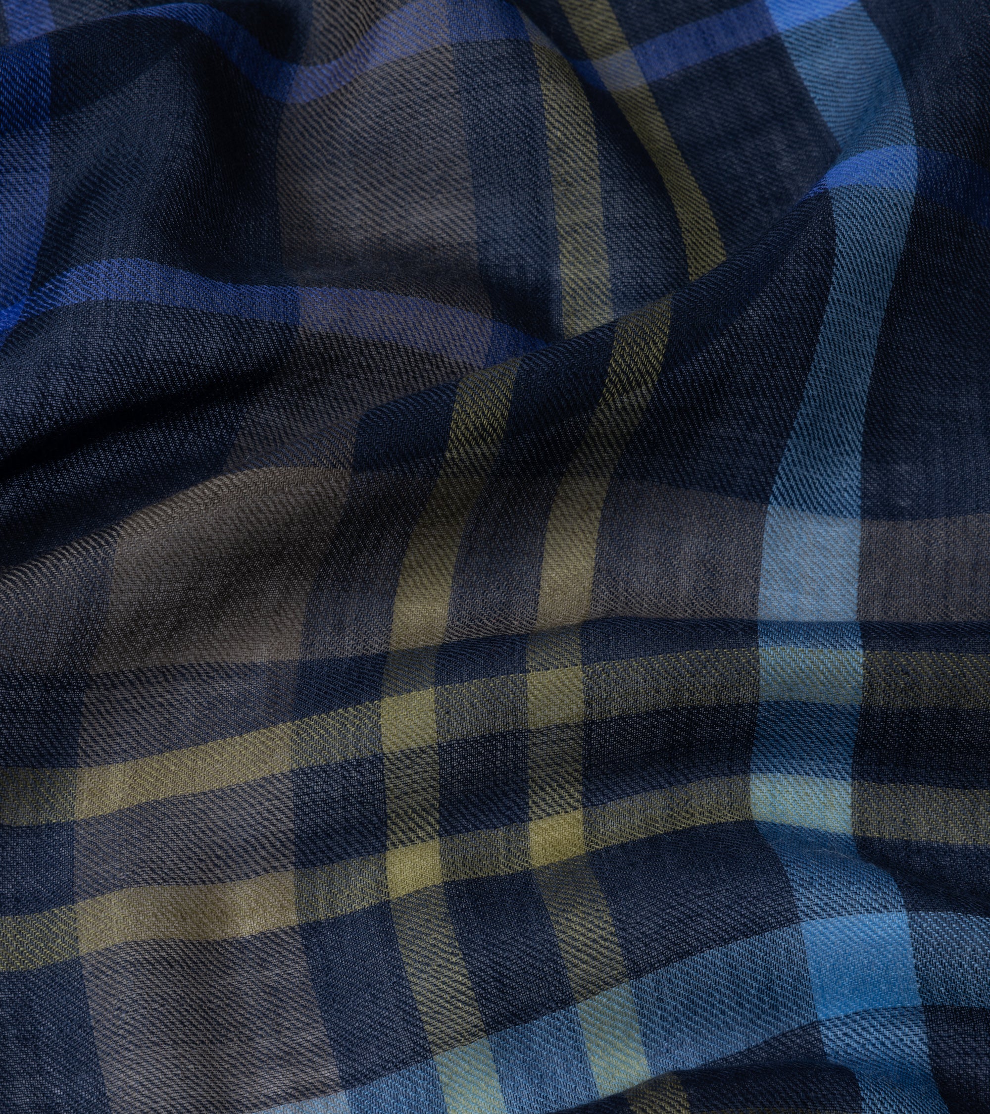 A close-up of a plaid fabric with a textured weave, featuring navy blue, slate gray, light blue, and muted olive green stripes.
