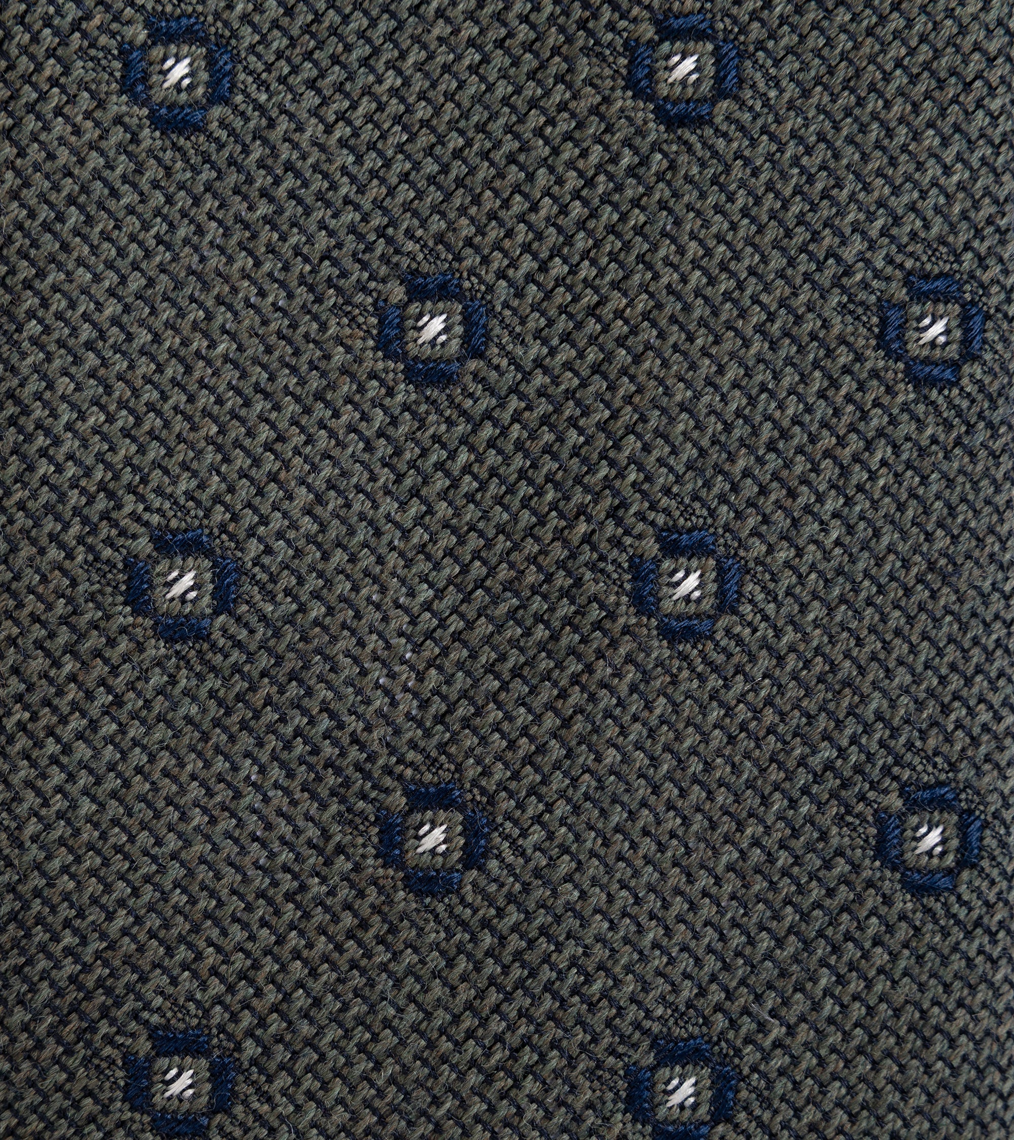 Close-up of a woven necktie fabric  in dark gray, featuring a repeating pattern of small blue geometric medallions with white center details.