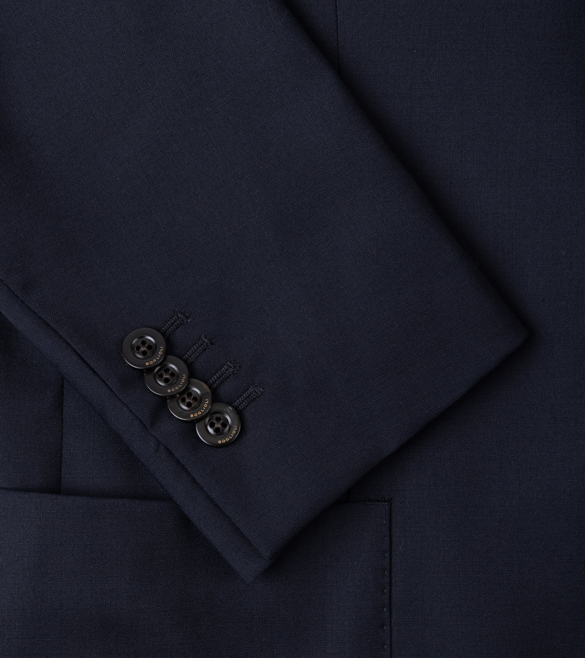 Close-up of a dark navy blue suit jacket or blazer sleeve, showing the fabric texture, a buttoned cuff with four buttons, and part of a pocket.