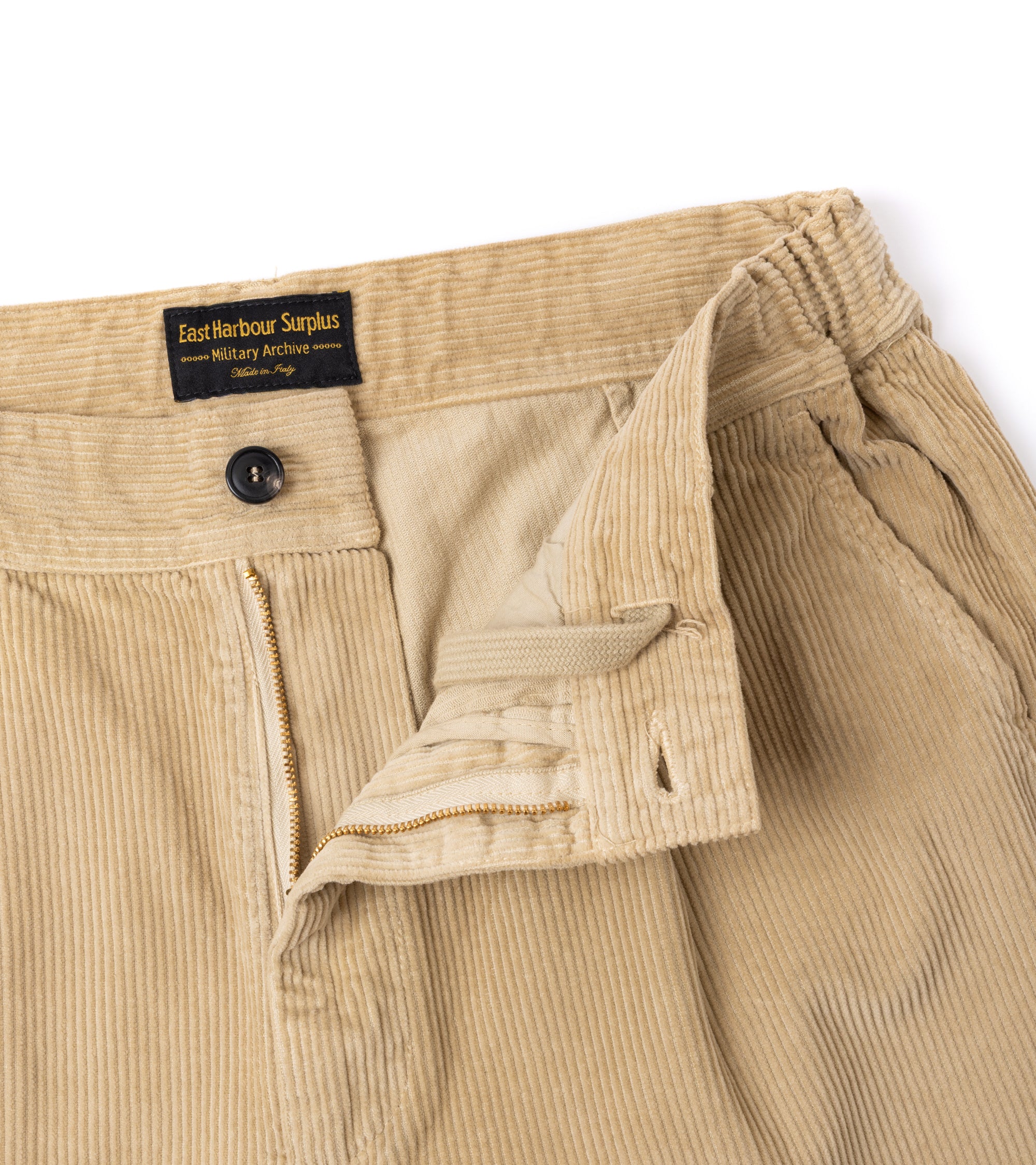Close-up of beige corduroy trousers showing the waistband, button closure, zipper and inner drawstring.