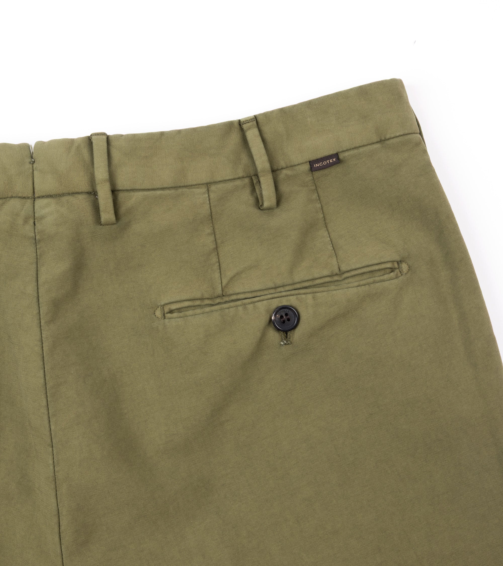 Close-up of olive green trousers showing the waistband, belt loops, a rear welt pocket with a button closure, and a small dark brand tab near the waistband.