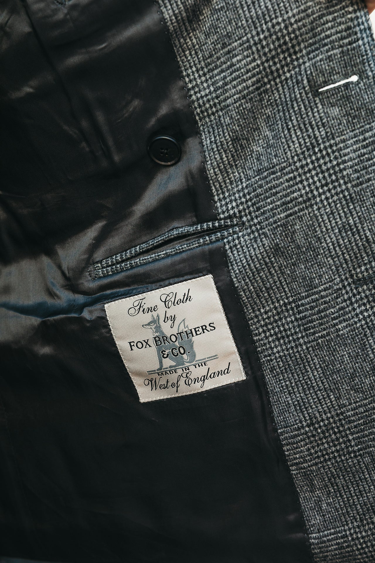 Close-up of a suit label on a black and gray checkered jacket with 'Fox Brothers & Co' branding.