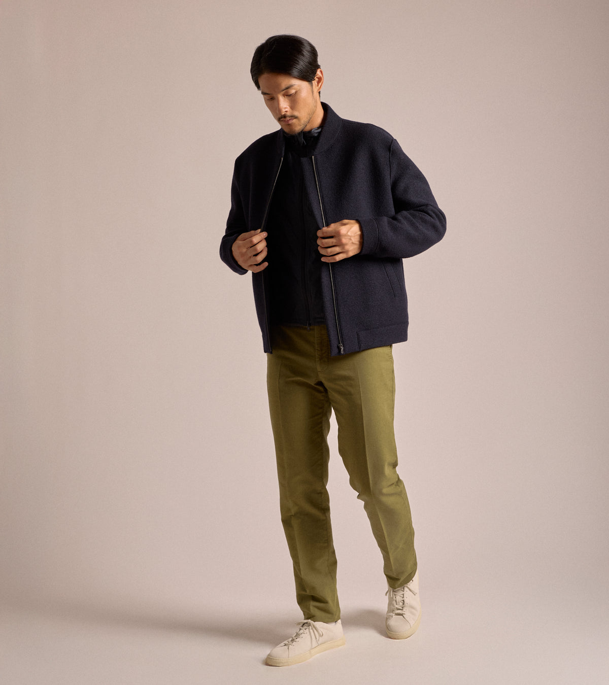 A model wearing teh Harris Wharf Boiled Wool Bomber Jacket in Navy Blue styled  with a dark shirt, olive green trousers and off-white sneakers.